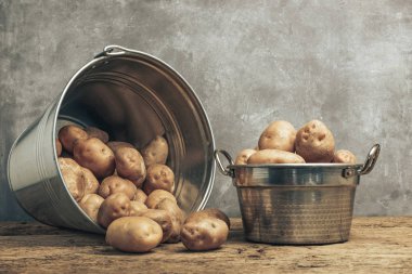 Eski bir meşe ahşap masa ve güzel gri duvar arka plan üzerinde gümüş sepet taze patates.