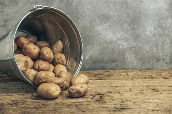 Fresh potatoes in silver basket on a old oak wooden table and beautiful gray wall background.