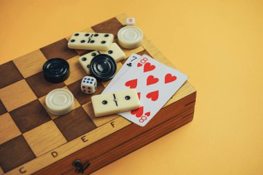 Çeşitli masa oyunları satranç tahtası, iskambil kartları, turuncu arka planda domino taşları..