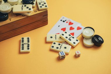 Çeşitli masa oyunları satranç tahtası, iskambil kartları, turuncu arka planda domino taşları..