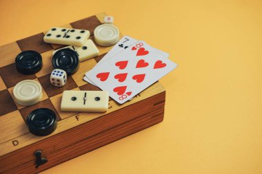 Çeşitli masa oyunları satranç tahtası, iskambil kartları, turuncu arka planda domino taşları..