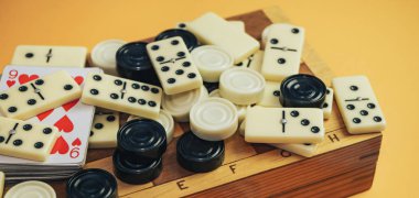 Çeşitli masa oyunları satranç tahtası, iskambil kartları, turuncu arka planda domino taşları..