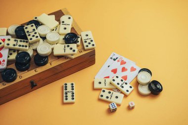 Çeşitli masa oyunları satranç tahtası, iskambil kartları, turuncu arka planda domino taşları..