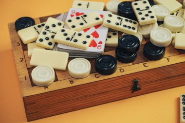 Çeşitli masa oyunları satranç tahtası, iskambil kartları, turuncu arka planda domino taşları..