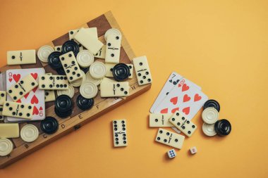 Çeşitli masa oyunları satranç tahtası, iskambil kartları, turuncu arka planda domino taşları..
