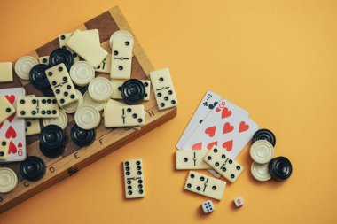 Çeşitli masa oyunları satranç tahtası, iskambil kartları, turuncu arka planda domino taşları..