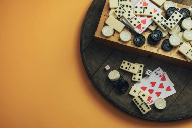 Çeşitli masa oyunları, satranç tahtaları, iskambil kağıtları, eski tahta masa turuncu arka plan dominoları..