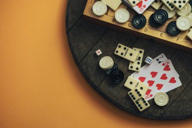 Çeşitli masa oyunları, satranç tahtaları, iskambil kağıtları, eski tahta masa turuncu arka plan dominoları..