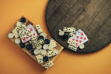 Çeşitli masa oyunları, satranç tahtaları, iskambil kağıtları, eski tahta masa turuncu arka plan dominoları..