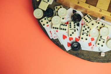 Çeşitli masa oyunları, satranç tahtası, iskambil kağıtları, eski ahşap masa şeftali arka planında domino taşları.