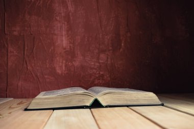 Open Holy Bible on a old wooden table. Beautiful red wall background.	
