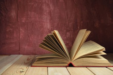 Kırmızı ahşap bir masada eski güzel bir kitap ve arkasında koyu kırmızı bir duvar var..
