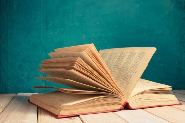 Kırmızı ahşap bir masa ve koyu yeşil bir arka plan üzerinde eski ve güzel bir kitap..