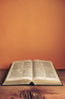 Open Holy Bible on a old wooden table. Beautiful orange wall background.	