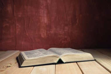 Open Holy Bible on a old wooden table. Beautiful red wall background.	