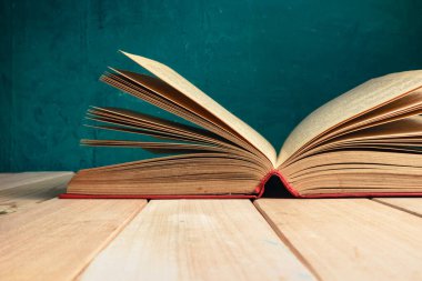 Kırmızı ahşap bir masa ve koyu yeşil bir arka plan üzerinde eski ve güzel bir kitap..