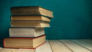 Eski ahşap bir masanın üzerindeki eski kitaplar. Güzel yeşil duvar arkaplanı.