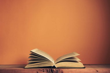 Meşe ağacından bir masanın üzerinde eski, açık bir kitap. Arkadaki turuncu duvarın arkaplanı.