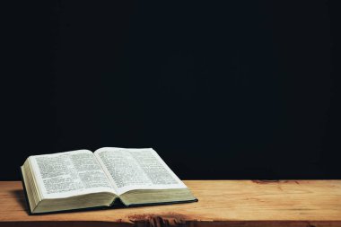Open Holy Bible on a red old wooden table. Beautiful Black wall background.	