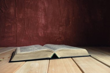 Open Holy Bible on a old wooden table. Beautiful red wall background.	