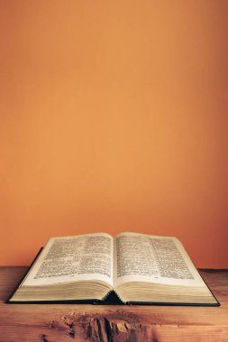 Open Holy Bible on a old wooden table. Beautiful orange wall background.	