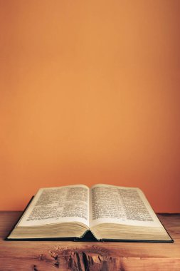 Open Holy Bible on a old wooden table. Beautiful orange wall background.	 clipart