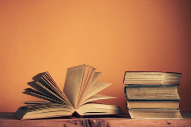 Eski ahşap bir masanın üzerindeki eski kitaplar. Güzel turuncu duvar arkaplanı.