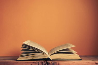Meşe ağacından bir masanın üzerinde eski, açık bir kitap. Arkadaki turuncu duvarın arkaplanı.