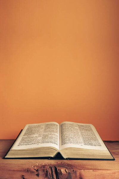 Open Holy Bible on a old wooden table. Beautiful orange wall background.	