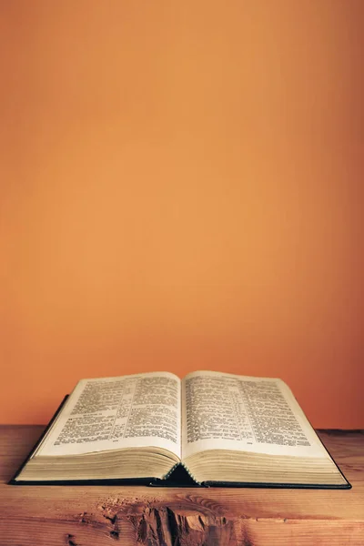 Open Holy Bible Old Wooden Table Beautiful Orange Wall Background Лицензионные Стоковые Фото