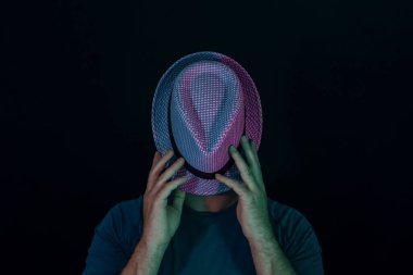 Genç adam yüzünü neon ışığıyla kaplamış siyah bir şapkayla. Minimalizm retro tarzı konsept.
