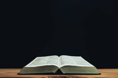 Open Holy Bible on a red old wooden table. Beautiful Black wall background.	