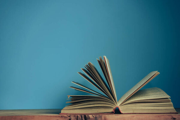 Beautiful open book on a red wooden table and blue wall background.