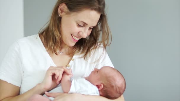 Žena drží v náručí novorozené dítě. Dítě se dívá na svou matku a úsměvy s bezzubými ústy. Matka a dítě. Den matek