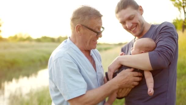Un nieto pequeño, abuelo y padre. Tres generaciones de hombres. Día de la familia. Un hombre entrega a su hijo recién nacido a su abuelo — Vídeo de stock