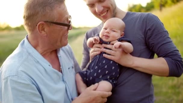 Famille multi-générations. Grand-père embrasse le pied d'un petit-fils. Trois hommes reposent sur la nature, près de la rivière. Coucher de soleil coloré — Video