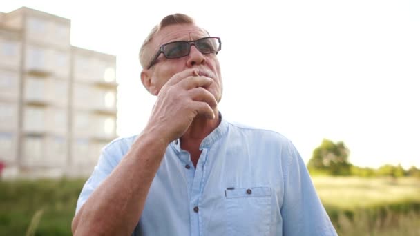 Um pensionista fora da cidade está nervoso e fumando. Problemas da idade da reforma. Danos ao fumo — Vídeo de Stock