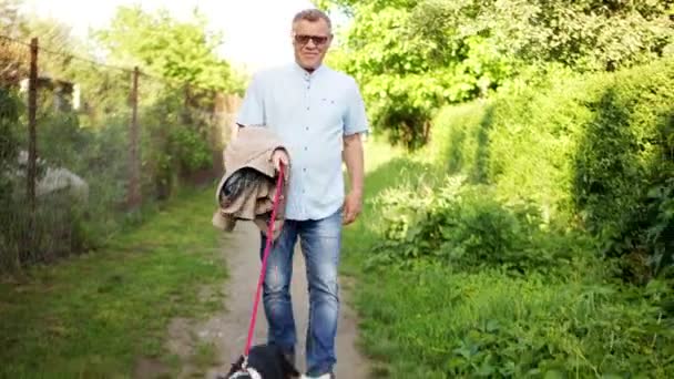 Een volwassen man loopt langs een landweg met zijn vrolijke hond. De hond springt hoog. Steadicam — Stockvideo