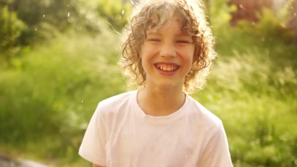 Un hermoso chico de pelo rizado está bajo la cálida lluvia de verano y sonríe. Día de los Niños. Felices Fiestas — Vídeo de stock