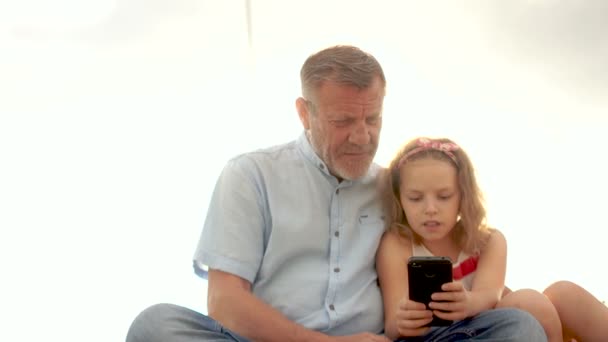 La dépendance à Internet. La fille et le grand-père regardent l'écran du téléphone. Loisirs en famille — Video