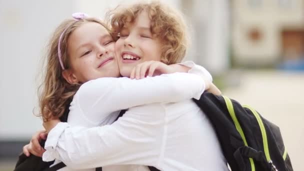Gli scolari si abbracciano dopo le vacanze estive. di nuovo a scuola. Giorno di conoscenza. Bei bambini, ragazzo e ragazza si abbracciano, sorridono, gli scolari sono vestiti con camicie bianche. — Video Stock