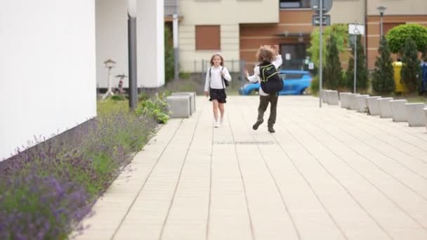 Um rapaz e uma rapariga no pátio da escola. A menina vai para casa, o menino tenta fazê-la rir, tolos ao redor, corre à frente dela. Dia dos tolos, amor escolar, primeiro amor, amizade escolar — Vídeo de Stock