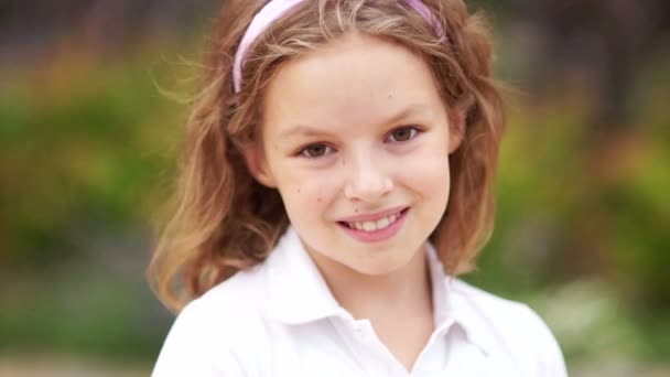 Közelről portré egy szép iskolás lány. A barna szemű szőke buzgón néz a kamerába, és kiegyenesíti a göndör haját — Stock videók