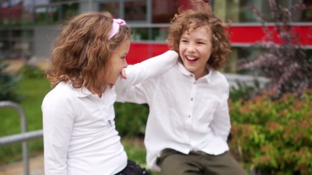 Schulfreundschaft. Ein Paar Teenager, ein Junge und ein Mädchen sitzen auf dem Geländer, das Mädchen hält ihre Hand auf der Schulter des Jungen. Kinder in weißen Hemden — Stockvideo
