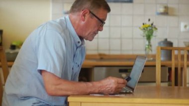 Bir bilgisayar ve telefon, onun mutfak bir masada oturan yaşlı bir adam çalışır. Gözlük vizyon ve koruma için