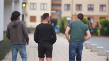 Genç erkekler şehirde yürüyüş. Arkadan görünüm. Üç adam mesafe içine gidin. Yaz yürüyüş, haftasonu, tatil