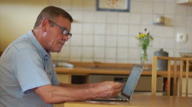 Olgun bir erkek bir dizüstü bilgisayar kullanarak faturaları ödüyor. Modern teknolojiler ve emeklilik yaşı halkı