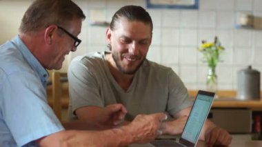 Babası bir yetişkin oğlu laptop yakınındaki mutfakta otururken konuşuyor. Oğlumun düzgün kesilmiş sakal var. Yaşlı insanların yaşam modern teknolojileri
