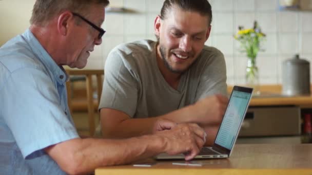 Ein junger Mann bringt seinem Vater bei, einen Laptop zu benutzen. lacht er fröhlich, gestikuliert emotional. Vatertag — Stockvideo