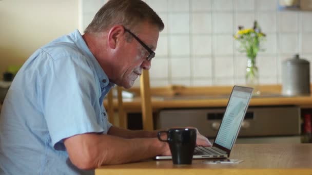 Um homem trabalha em casa com seu laptop, esfrega as mãos de forma justa, está satisfeito com o resultado, boas notícias. Emprego à distância, idosos, freelancer — Vídeo de Stock